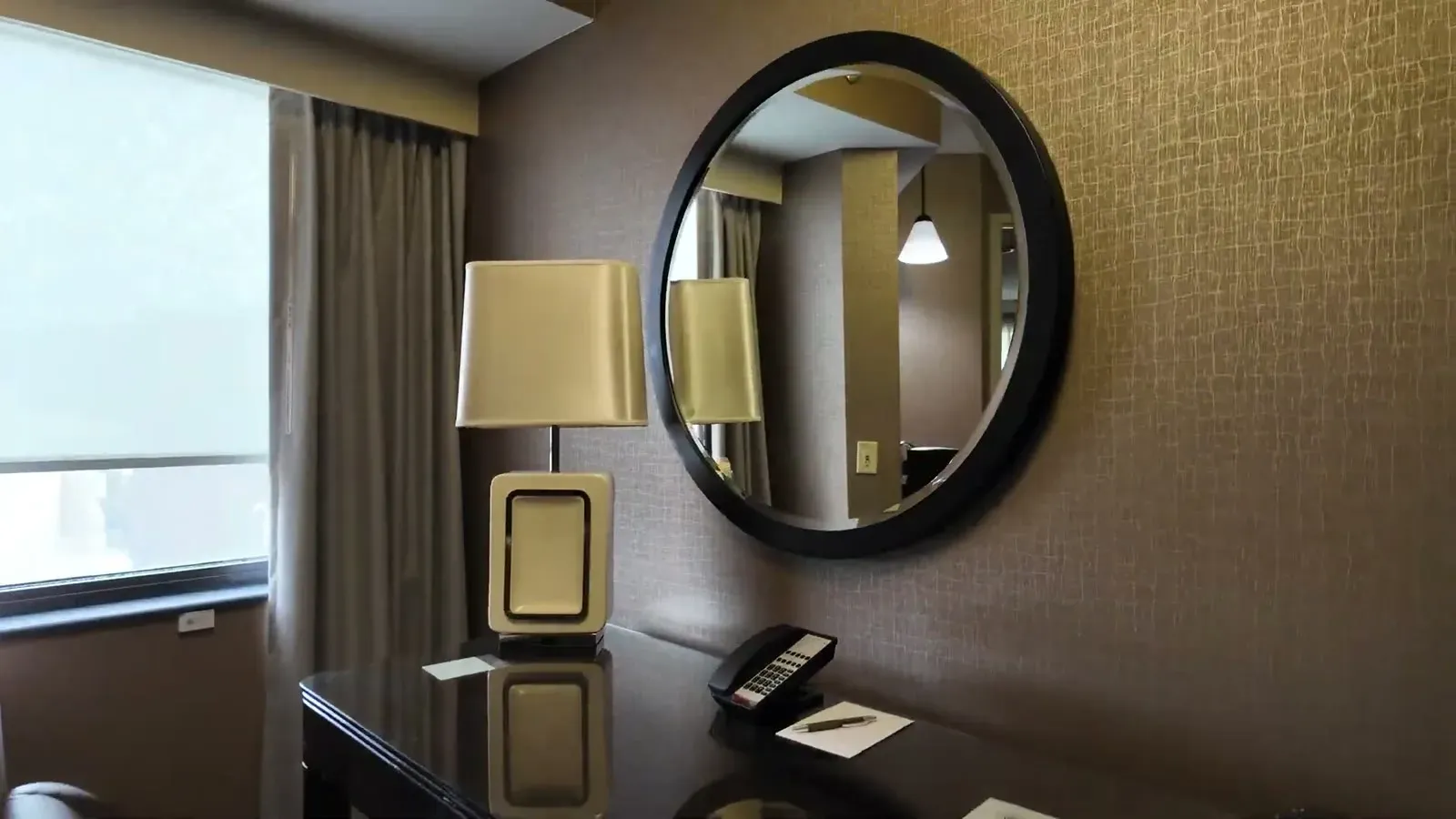 The living area of our suite at the Sheraton Suites Chicago O'Hare, with a desk, lamp, and round mirror in a separate room from the bed.