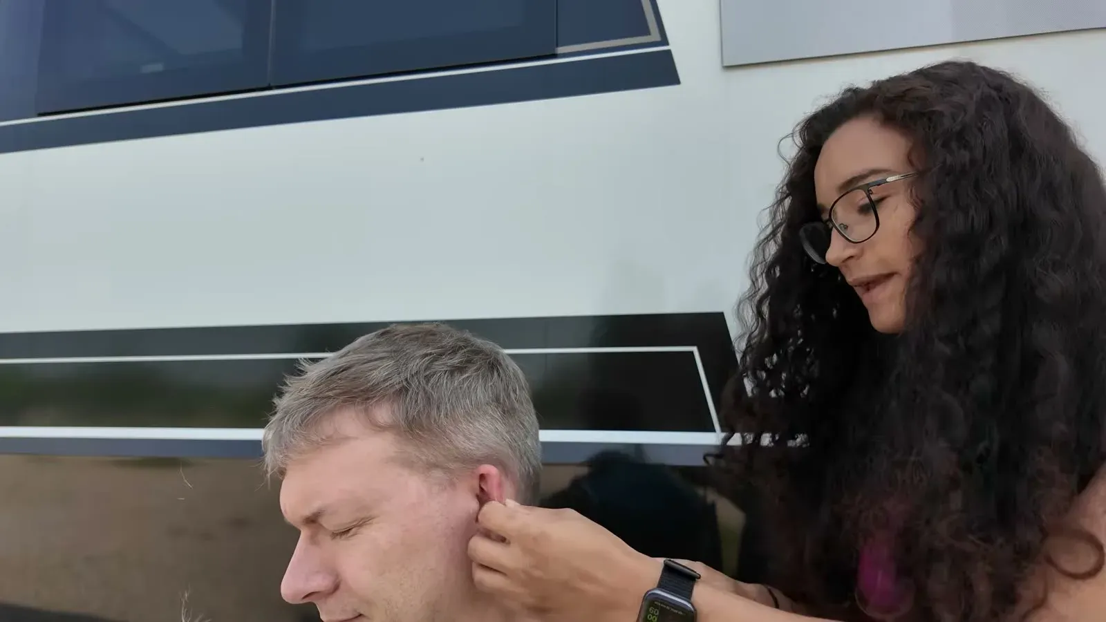 Fabiola tidying up around Nathan's ear with the clippers, right there beside the RV.