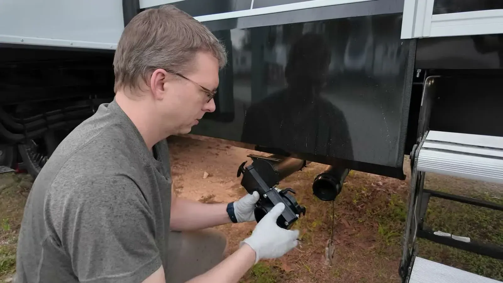 Nathan crouched at the sewer connection under the fifth wheel, fitting a Valterra twist-on waste valve with gloved hands.