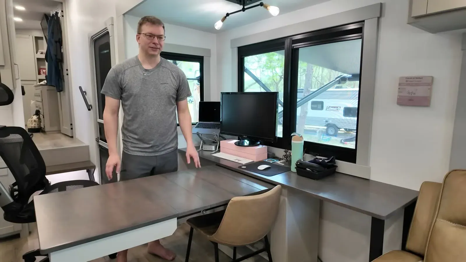 Nathan standing at the front office desk with the dinette extension pulled out, monitor and laptop set up by the big windows.