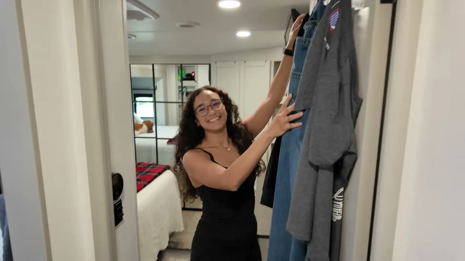 Fabiola grinning as she hangs clothes in the bedroom wardrobe, the closet that briefly tried to keep her, with the king bed behind.