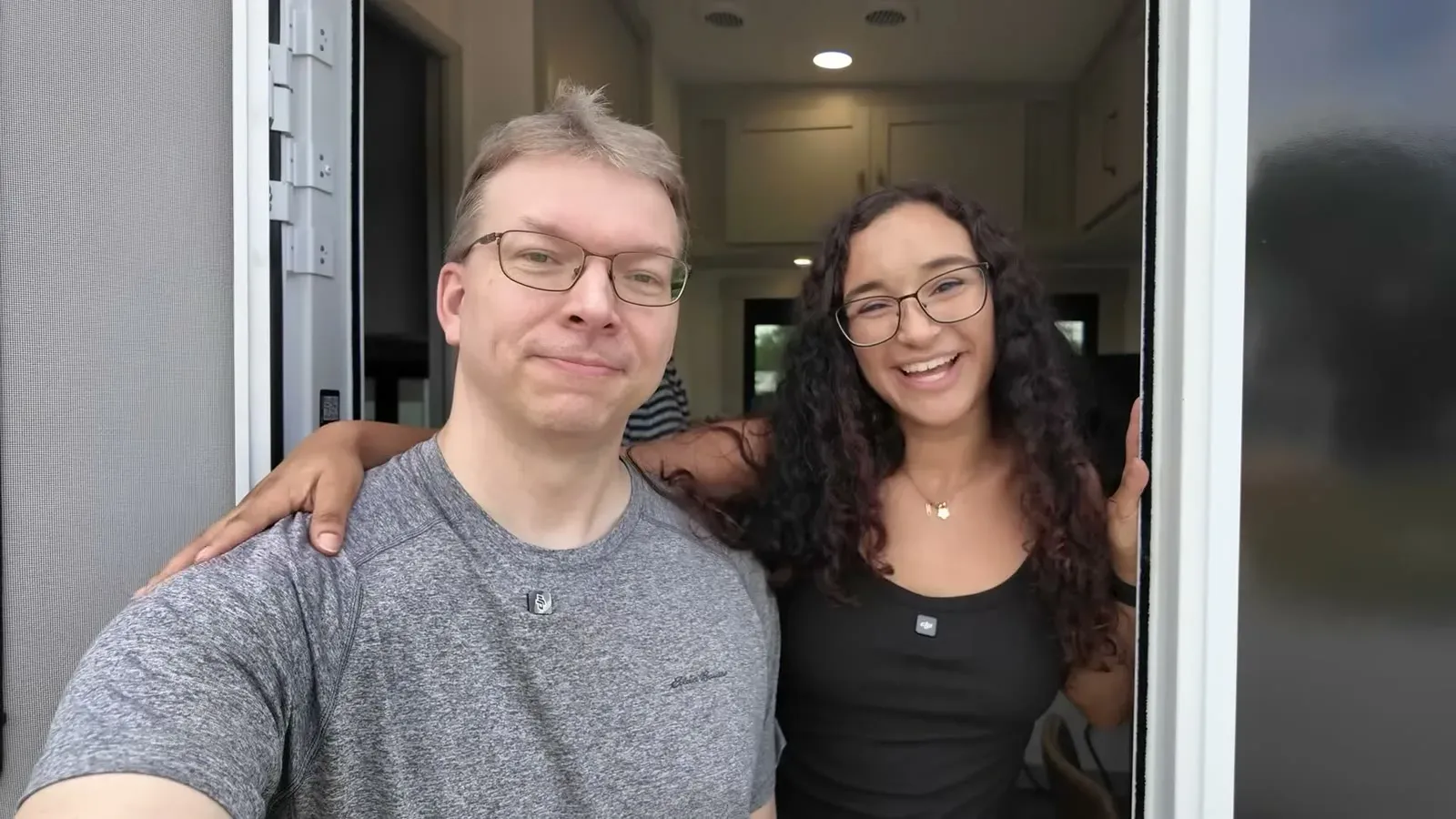 Nathan and Fabiola smiling in the entry doorway at the end of the tour of the fifth wheel they live in full time.