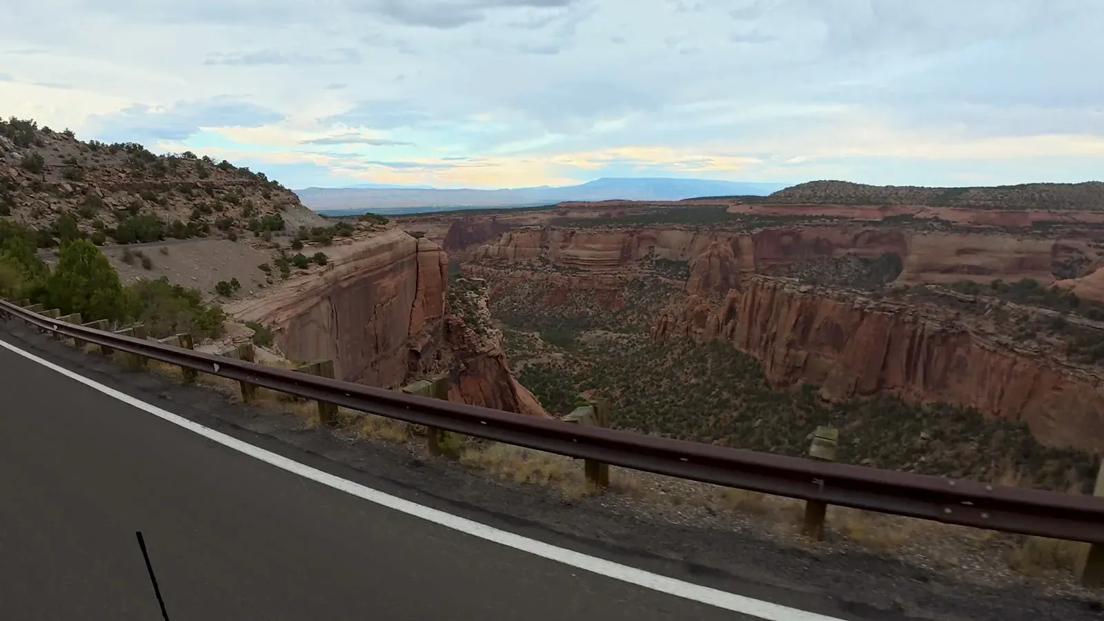 Rim Rock Drive running along the base of a red cliff, seen over the hood of our truck