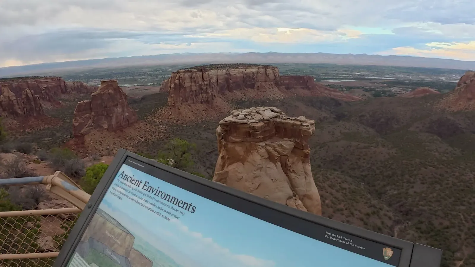Independence Monument rising from the canyon floor, with the overlook's interpretive sign in the foreground