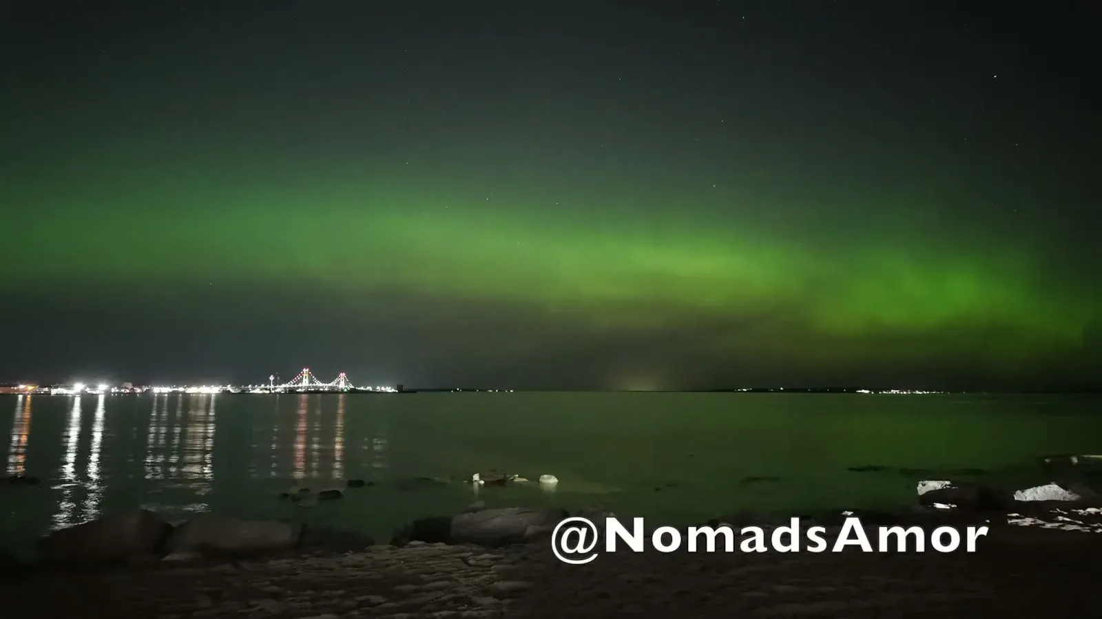 The first green glow of the aurora spreading over the Straits of Mackinac, with the bridge lights and their reflections off to the left of our beach.