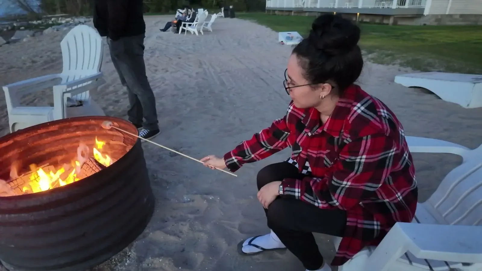 Fabiola roasting a marshmallow over a fire ring in the sand on the Lake Huron beach.