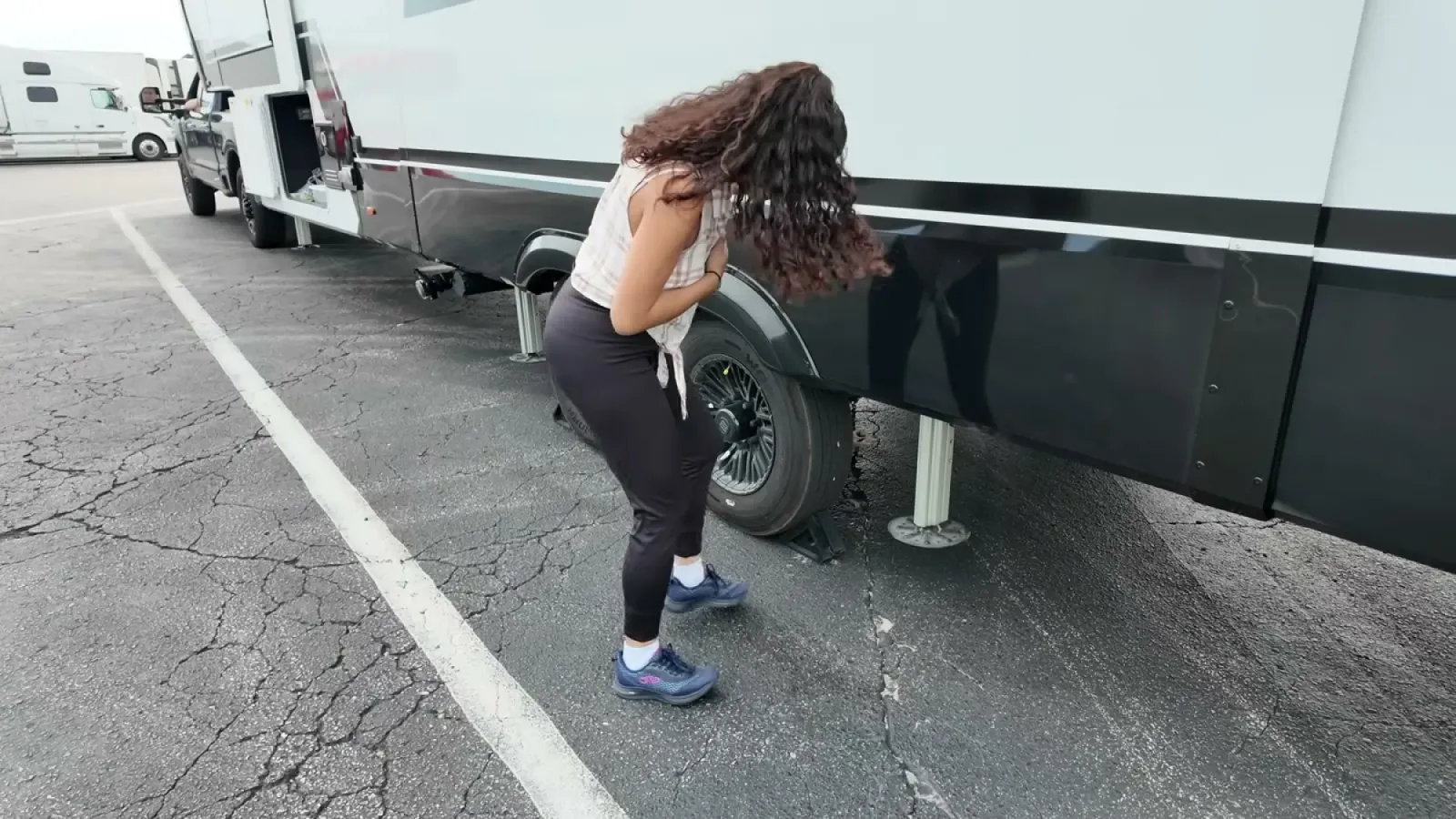 Fabiola placing wheel chocks by the fifth wheel tires in a travel center parking lot with the landing gear down