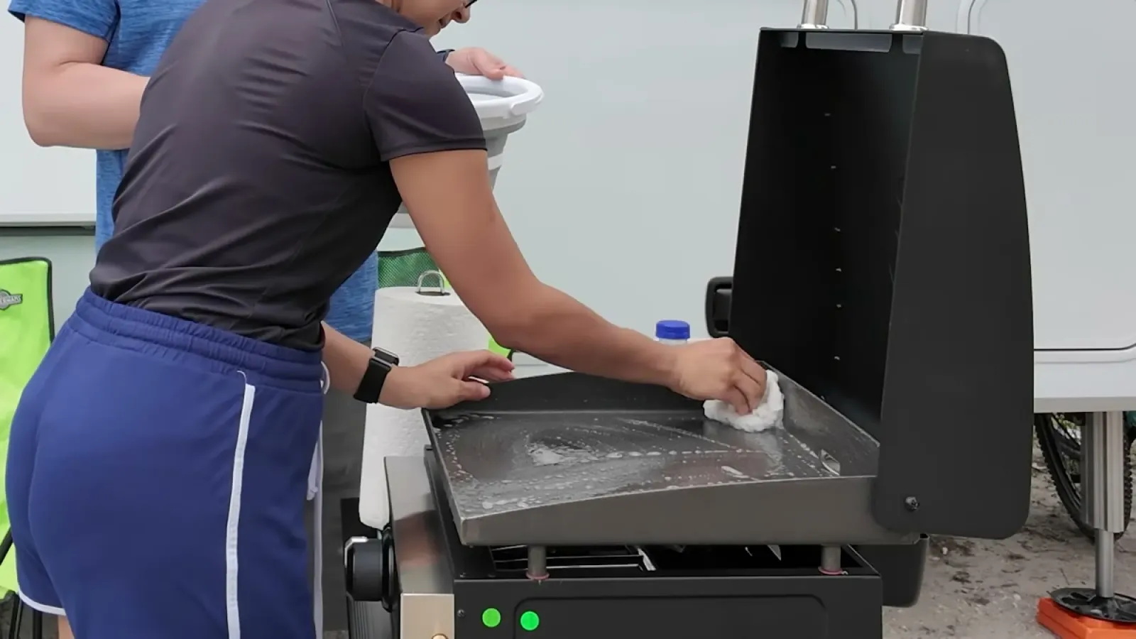 Fabiola scrubbing the bare gray cooktop of a new Blackstone 17 inch griddle with soapy water beside our fifth wheel