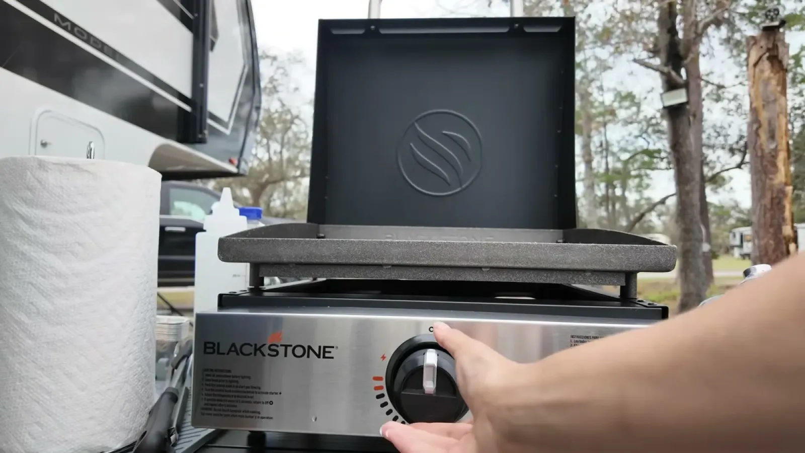 Hand turning the control knob on the Blackstone griddle with the hood open at our campsite