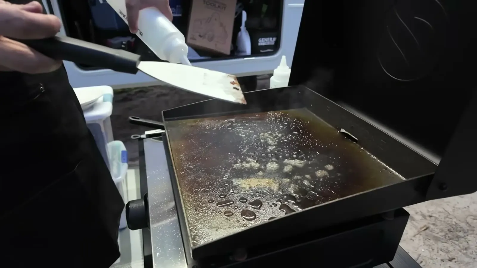 Scraper pushing water across the steaming Blackstone griddle surface during cleanup