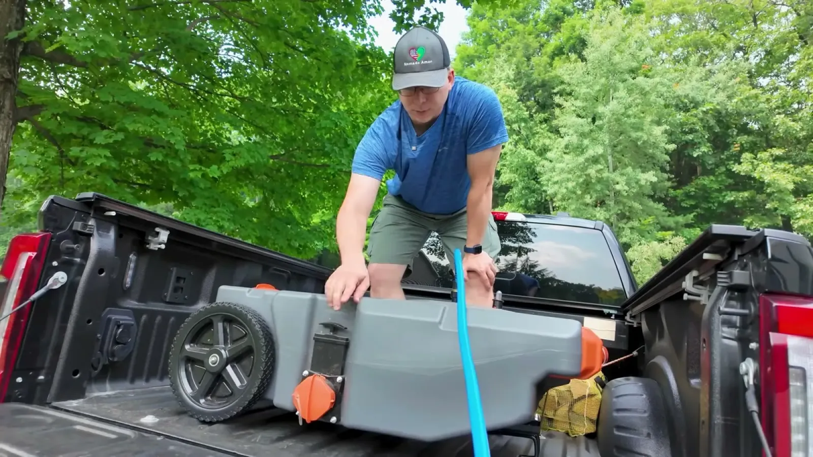 Nathan leaning over the tailgate checking the portable waste tote in the truck bed while it fills through a blue macerator hose