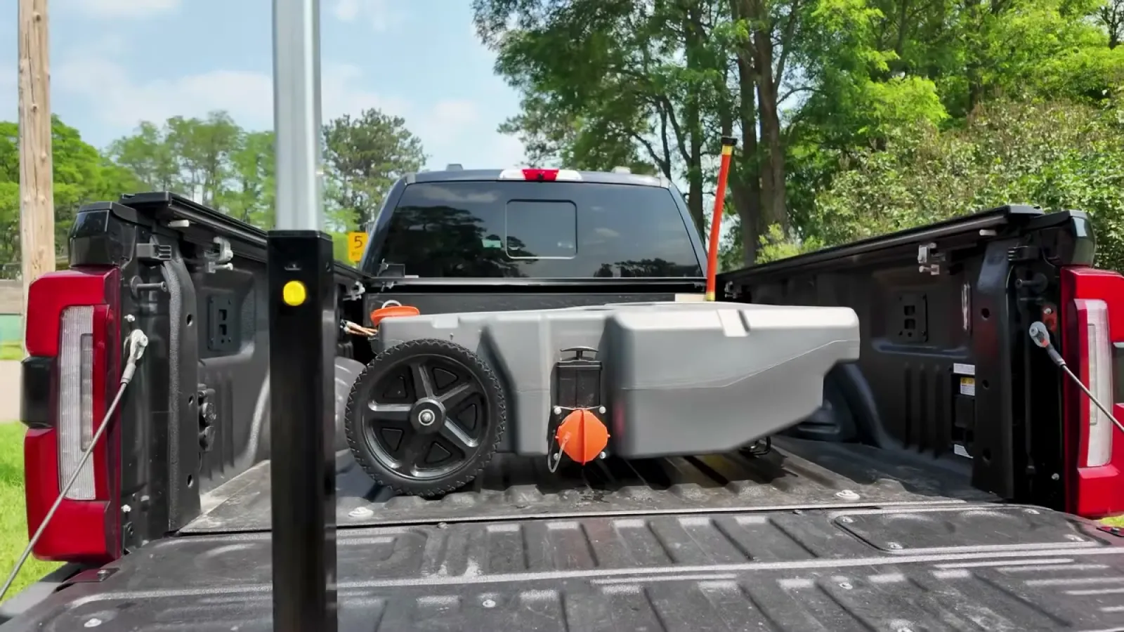 Gray Rhino tote tank with black wheels sitting in the black truck bed with the tailgate open at the campground dump station