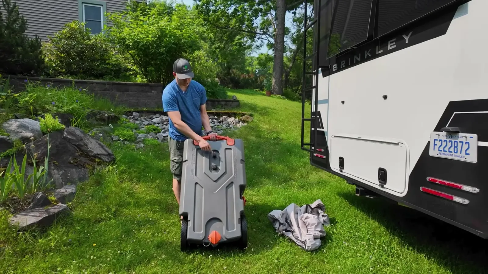 Nathan standing a gray Rhino portable waste tote upright on the grass next to the rear of the Brinkley fifth wheel