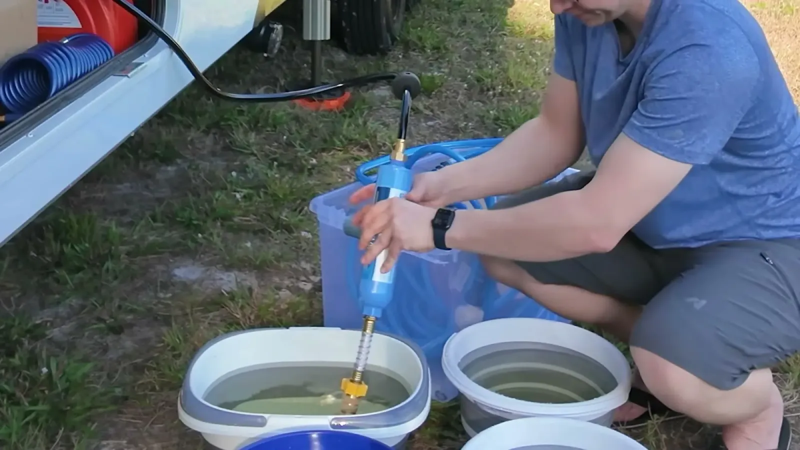Closeup of a blue hand siphon pump standing in a collapsible bucket of water next to the RV