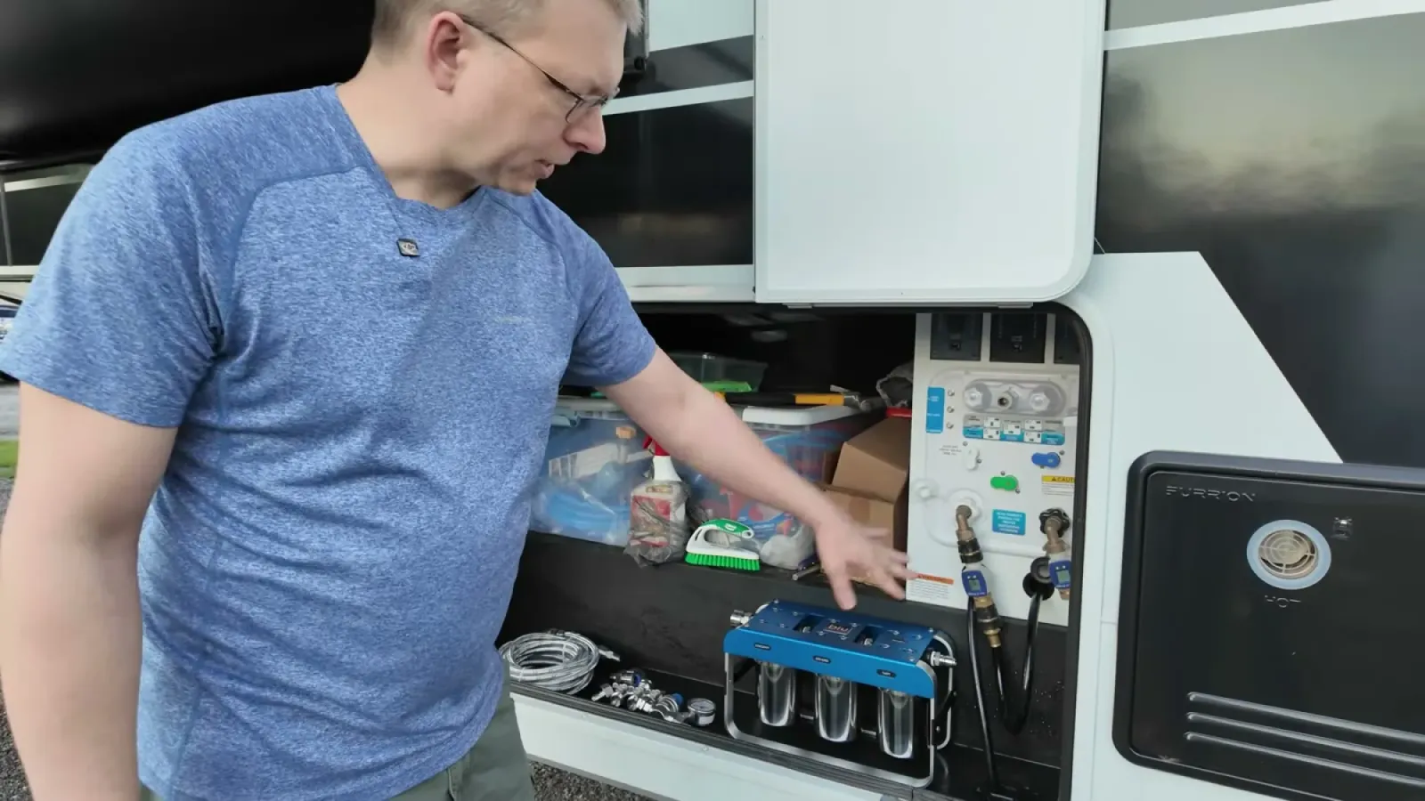 Nathan reaching into the open water bay of a Brinkley fifth wheel with the blue AR3 filter unit sitting below the water connections