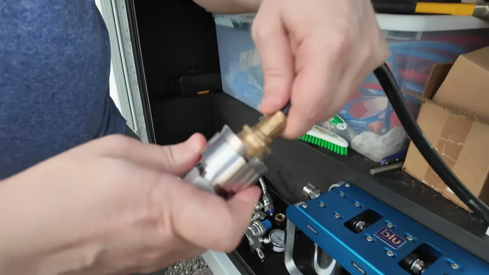 Hands attaching a brass and stainless steel quick connect fitting to a hose end above the blue AR3 filter unit in the water bay
