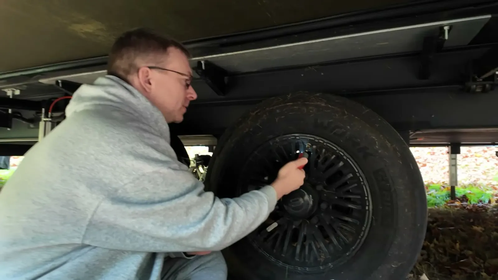 Nathan crouched under a fifth wheel pressing a digital tire pressure gauge onto the valve stem of a trailer tire
