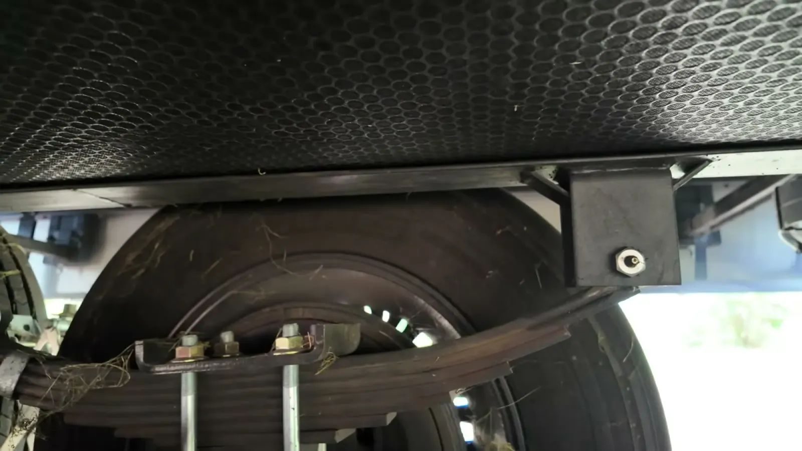 Underside view of a fifth wheel leaf spring, U-bolts, and spring hanger with a grease zerk fitting