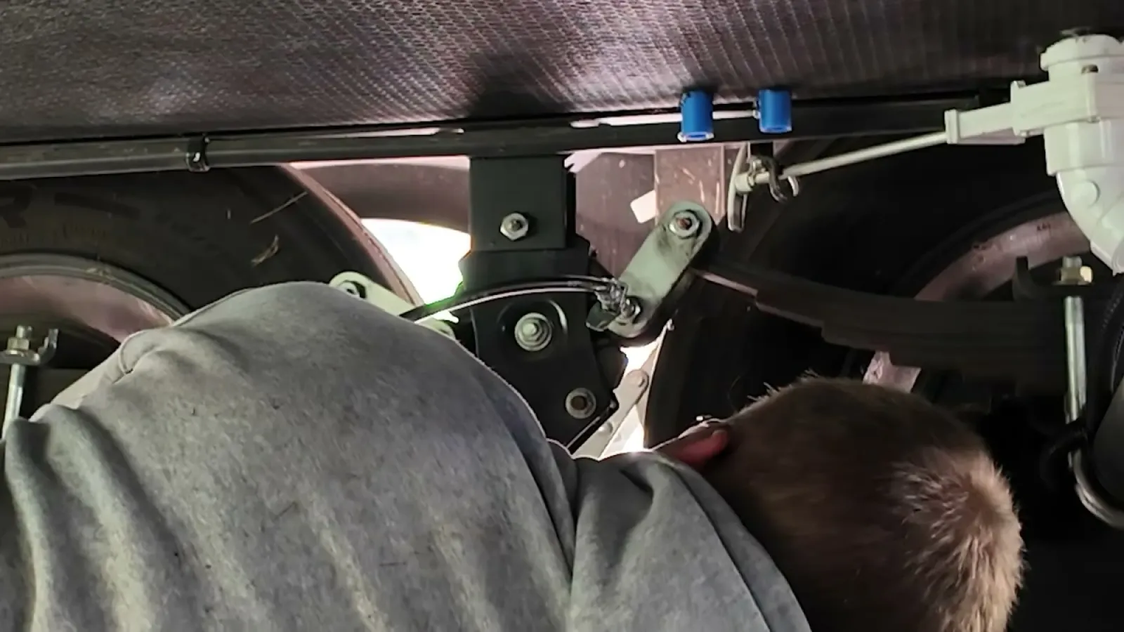 Nathan reaching up between the trailer wheels to grease a wet bolt fitting on the suspension shackle