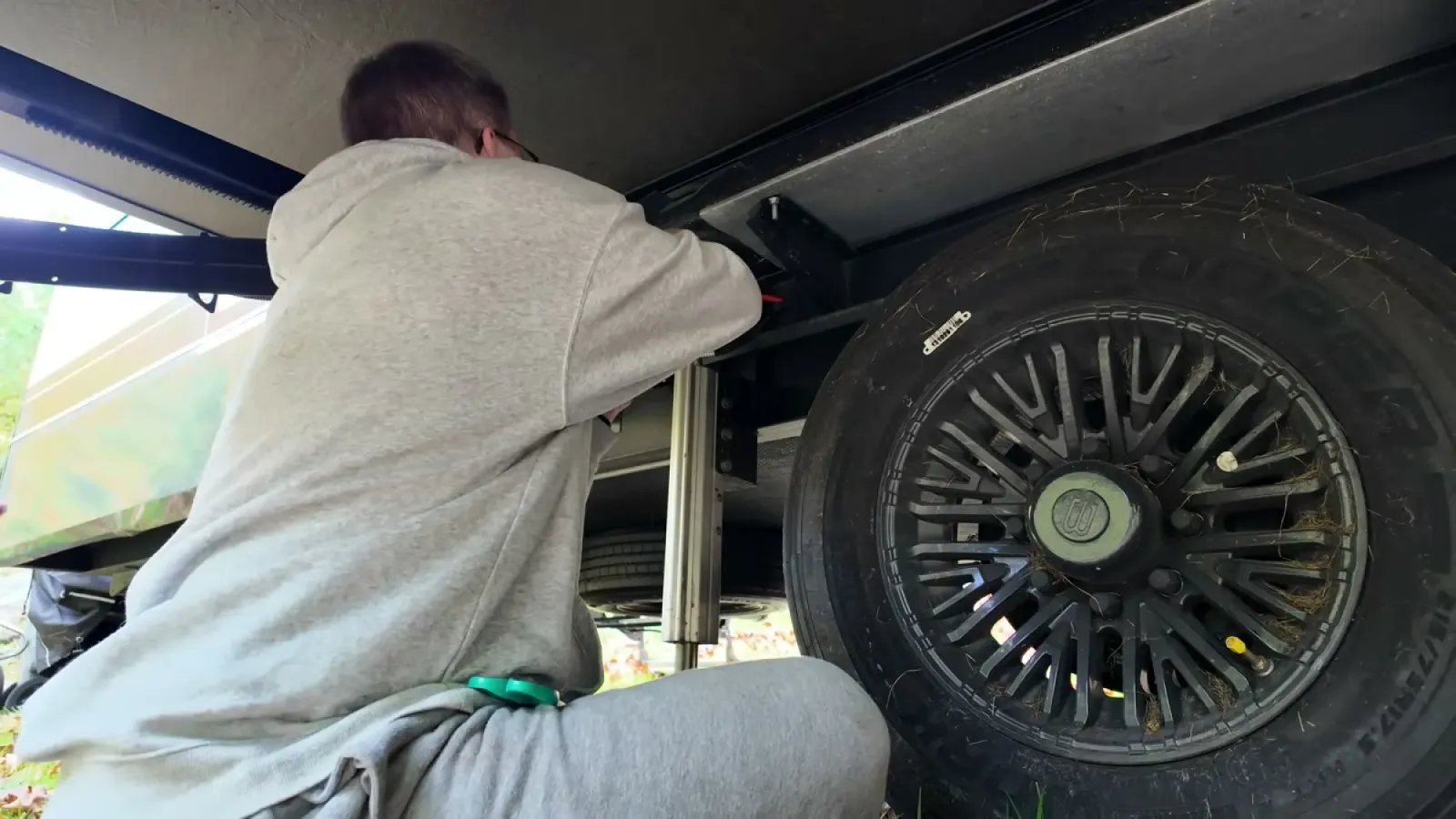 Nathan crouched under the fifth wheel beside a wheel, reaching up into the underbelly to seal an opening