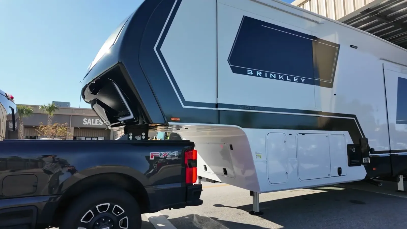 The nose of a Brinkley fifth wheel hitched over the bed of a Ford F-350, showing the clearance gap between the trailer overhang and the truck bed rails, landing gear still down