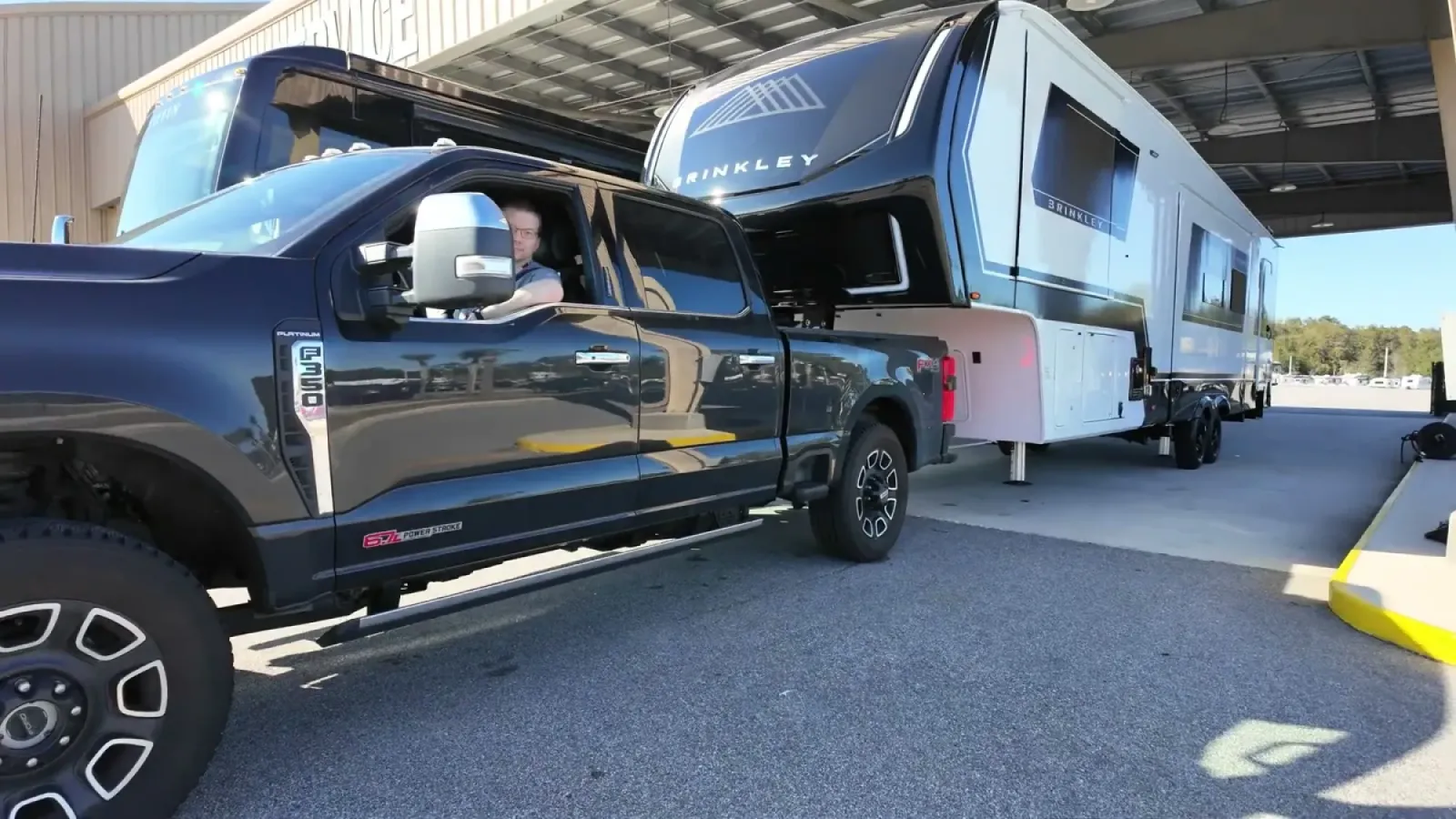 A Ford F-350 slowly pulling a Brinkley fifth wheel forward at the dealer lot with the front landing gear posts still extended near the ground