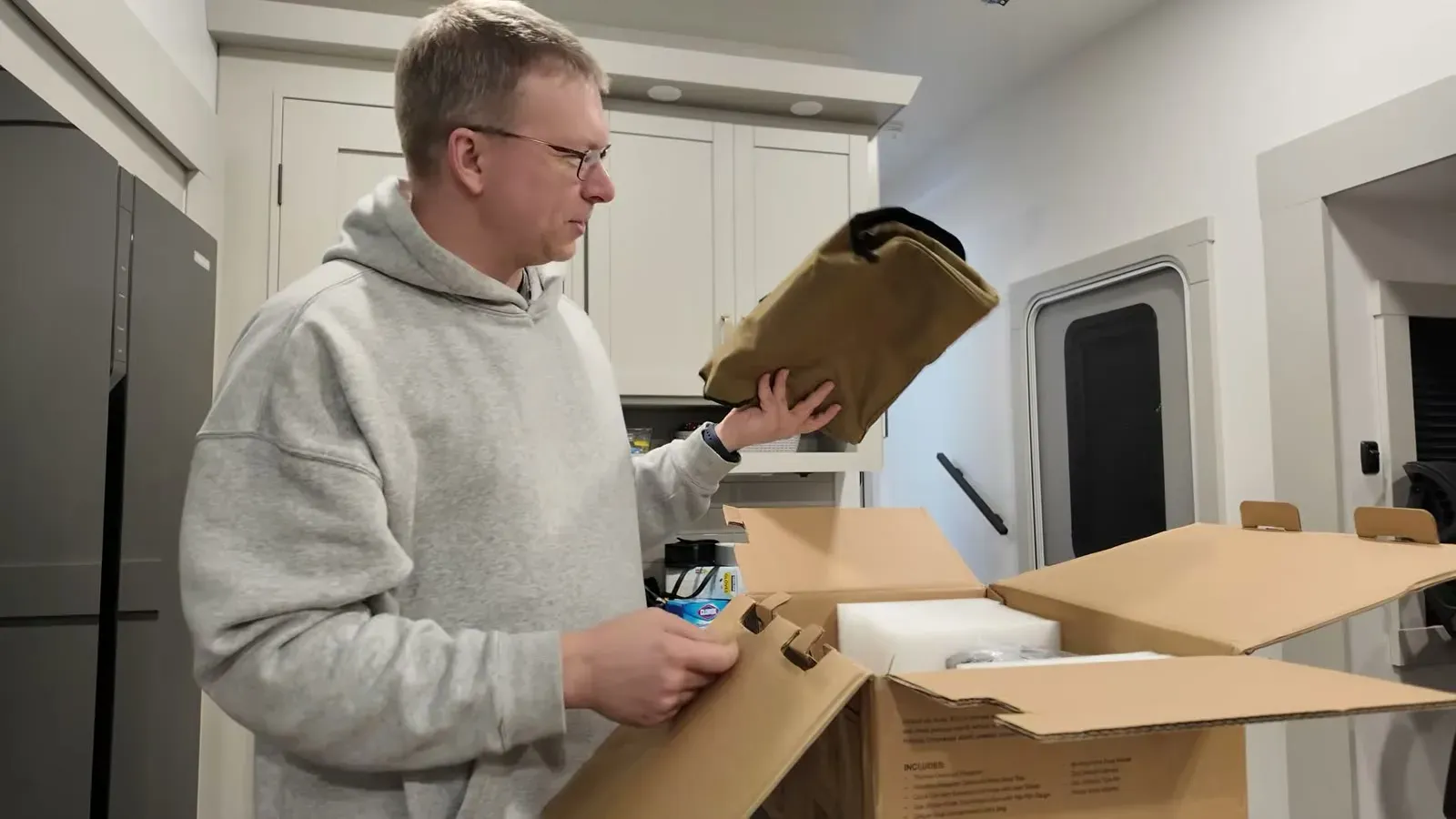 The tan soft-sided carrying case that comes with the VIAIR 400P compressor, held up by its handle next to the shipping box