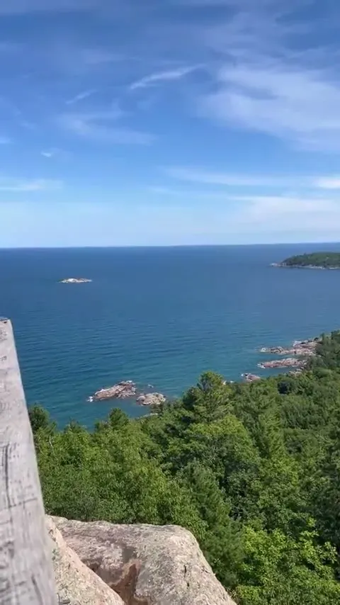 Lake Superior stretching to the horizon from the Sugar Loaf summit overlook, deep blue water beyond the rocky shoreline below.