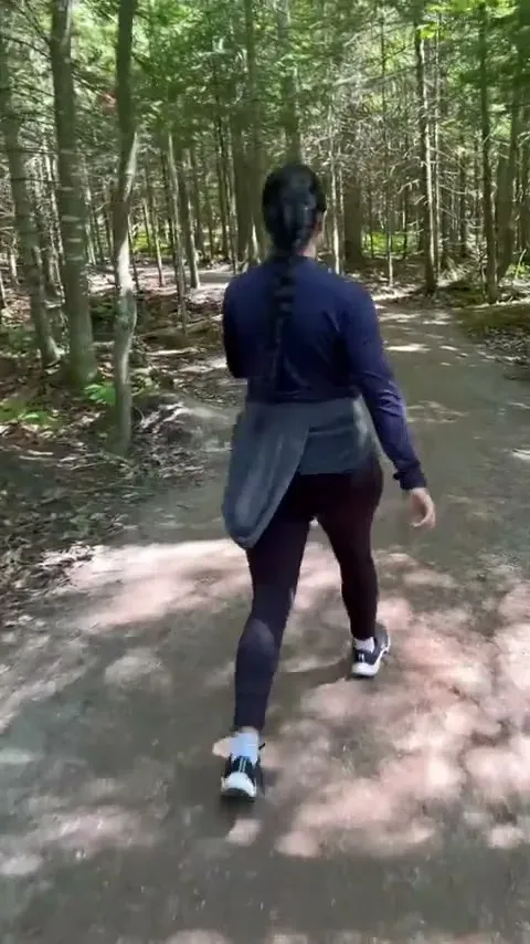 Fabiola walking the wide lower section of the Sugar Loaf trail through sunny green woods near the trailhead.