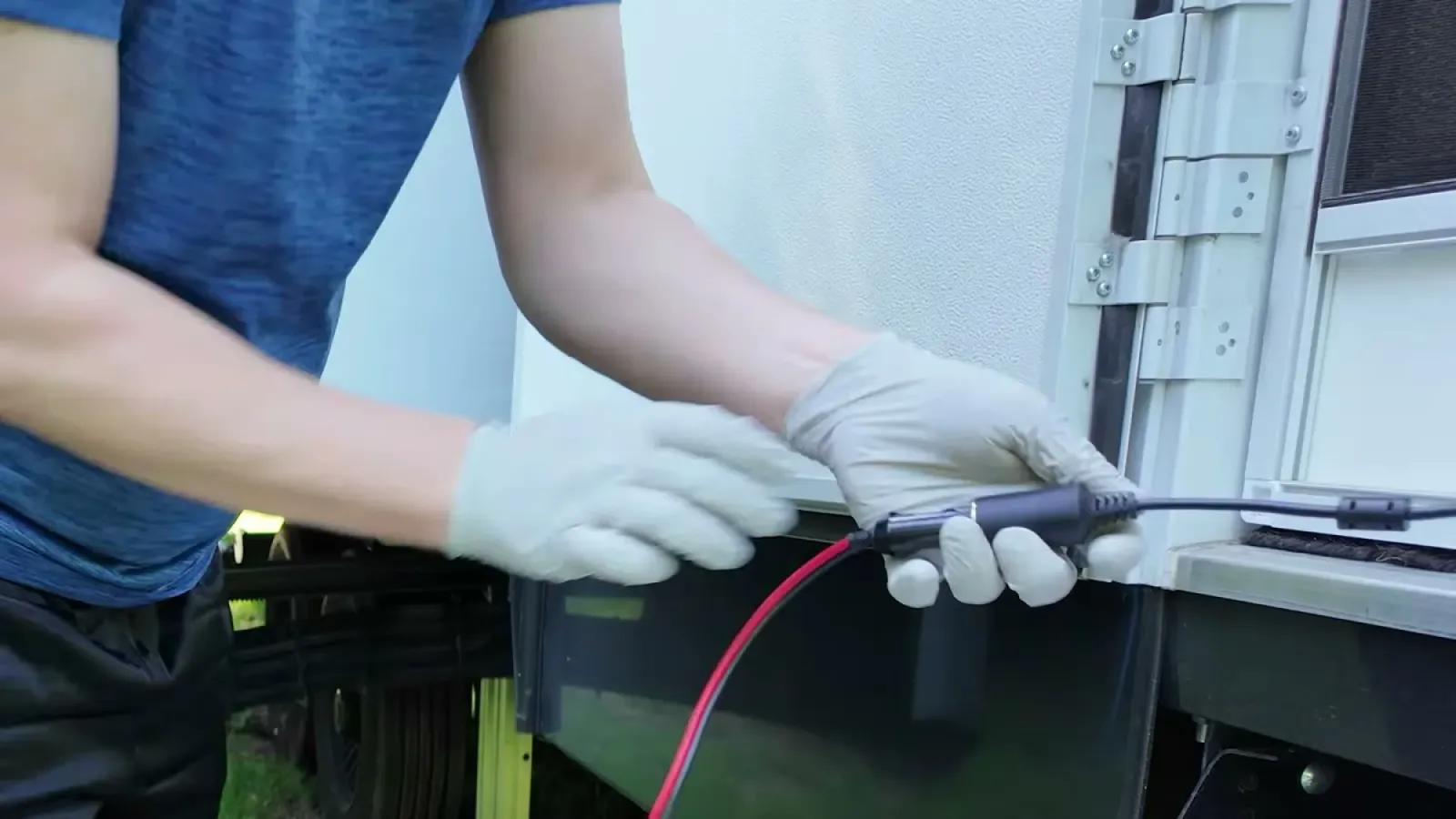 Gloved hands pushing the red macerator power cable into its connection under the side of the fifth wheel