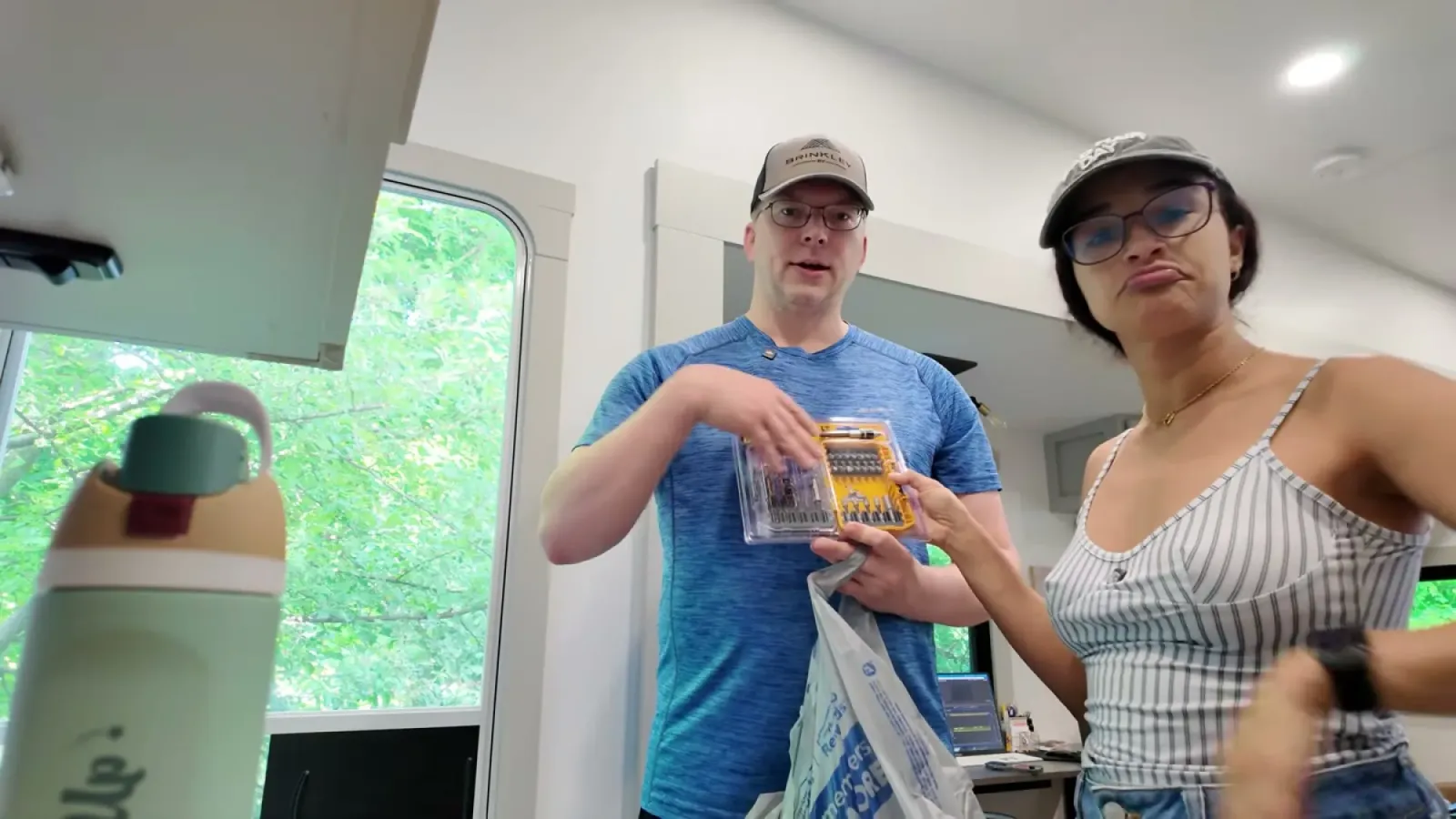 Nathan holding up a case of drill bits inside the RV while Fabiola looks at it with a skeptical expression
