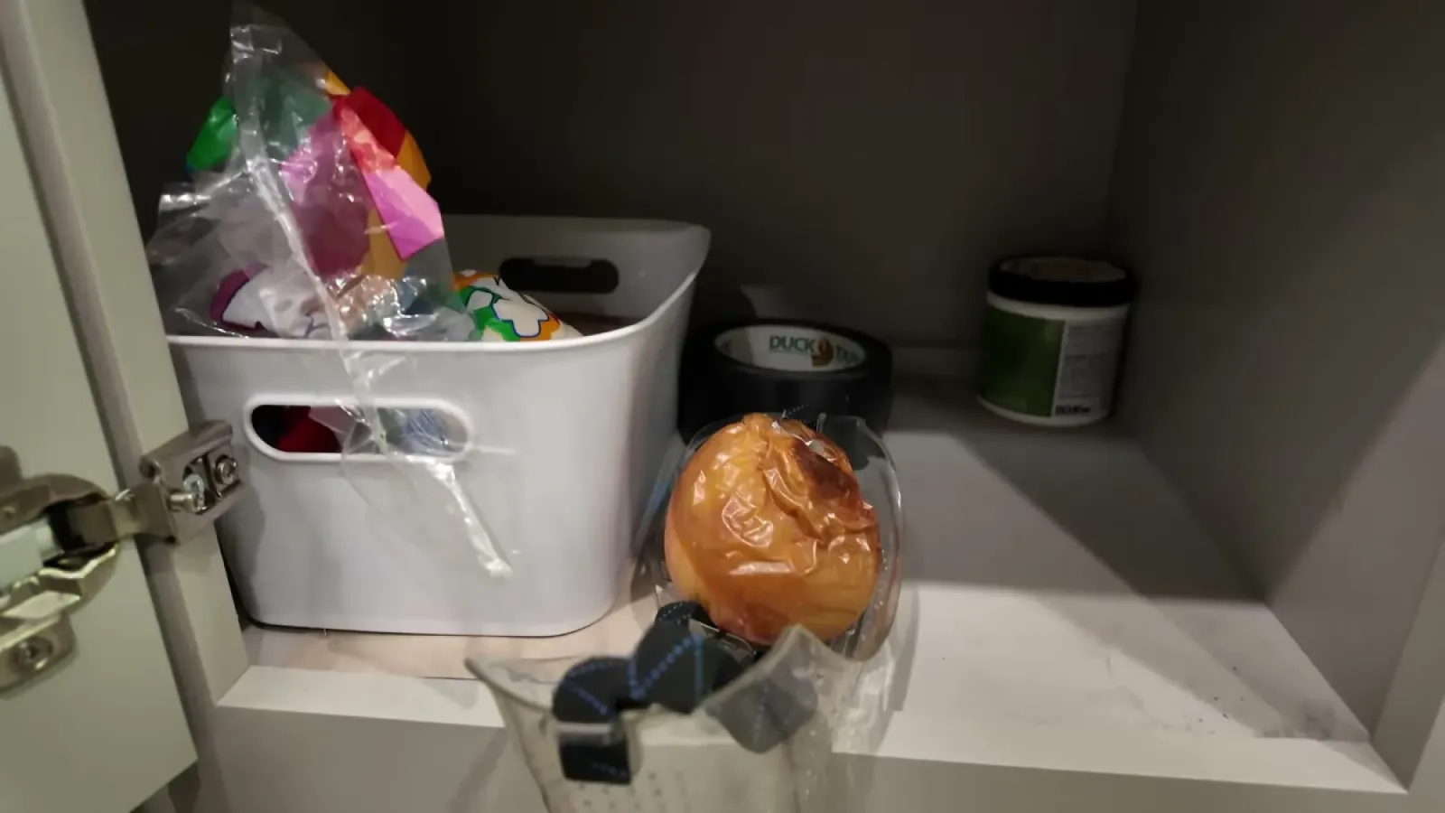 A brown moldy apple in a clear bag being lifted out of an RV cabinet next to a bin of s'mores supplies