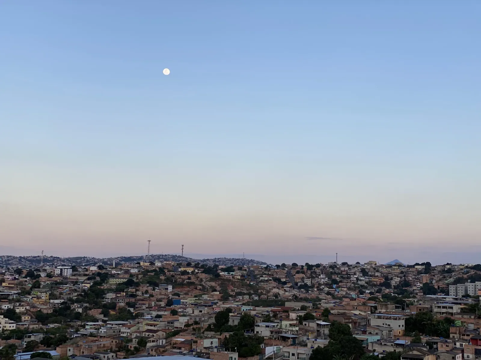 A vista da casa dos pais da Fabiola em Belo Horizonte, casas cobrindo os morros até o horizonte com a lua cheia nascendo ao entardecer.