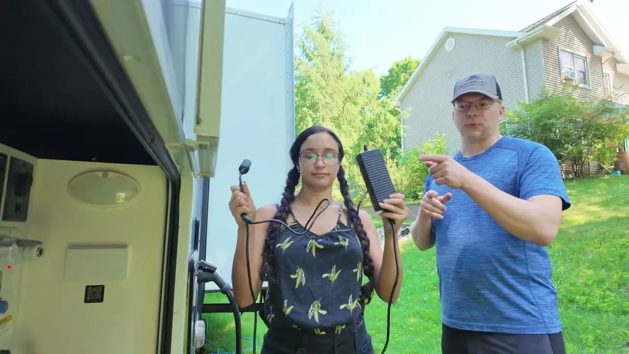Fabiola holding the replacement macerator power cord outside the RV while Nathan points at it