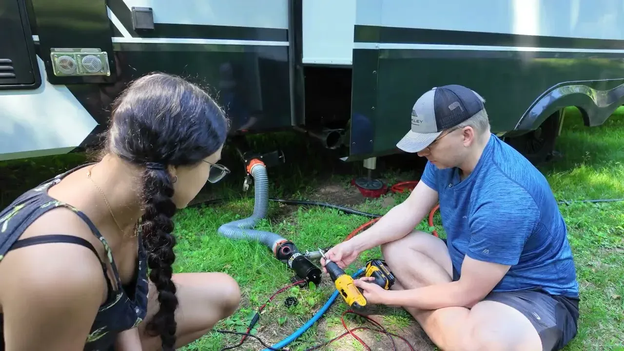 Nathan running a cordless drill on the back shaft of the macerator pump while Fabiola watches