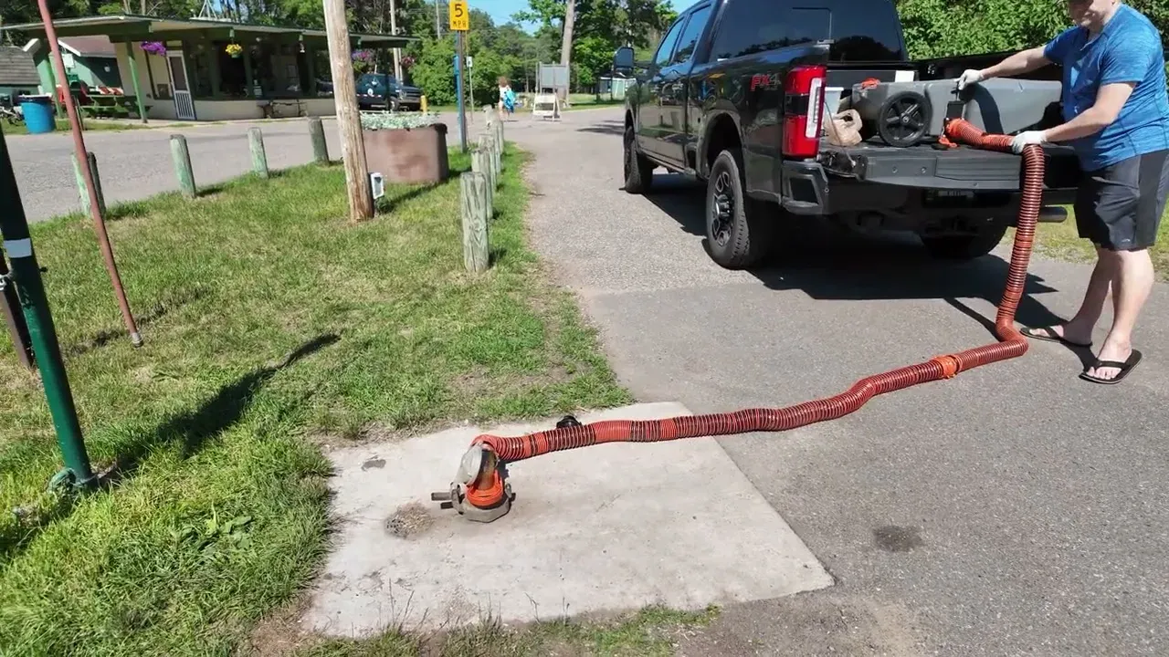 Sewer hose running from the portable waste tank in the truck bed down into the dump station inlet