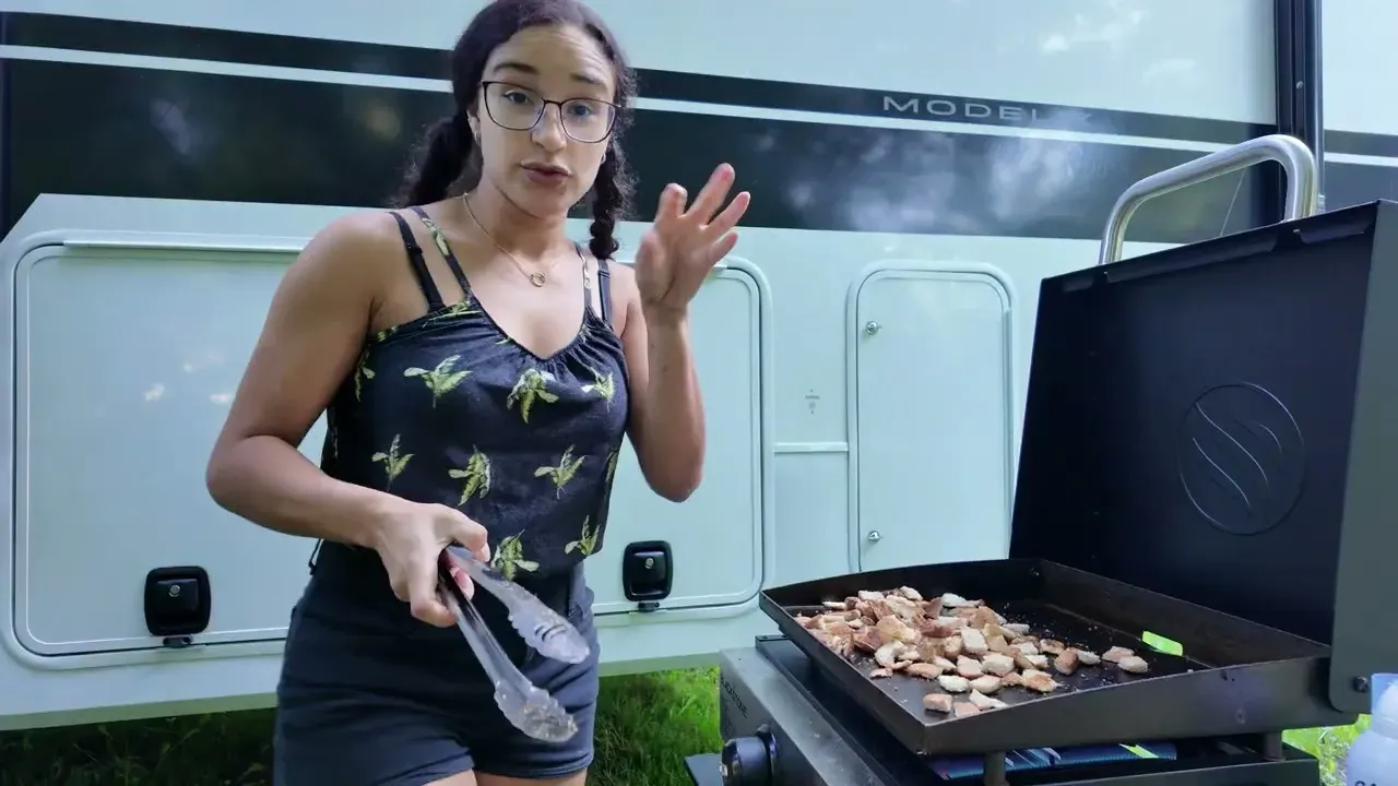 Fabiola cooking ground beef and bell peppers with tongs on the Blackstone griddle beside the fifth wheel