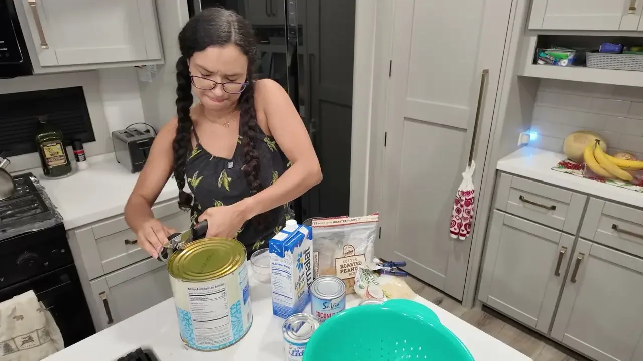 Fabiola opening a restaurant size can of white hominy on the RV kitchen counter next to milk and condensed milk