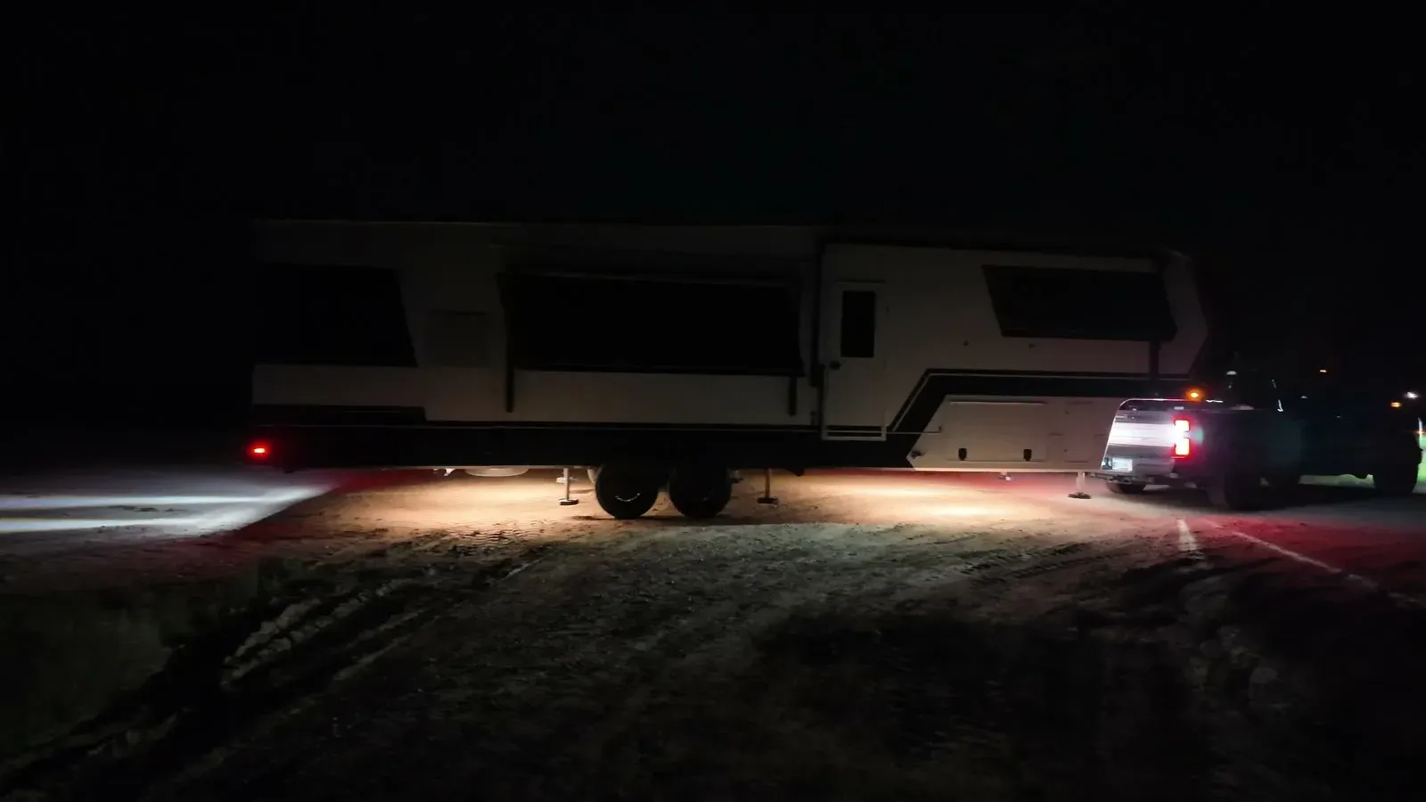 Our fifth wheel and truck lit red by the taillights on a dirt road at night, partway through the U-turn