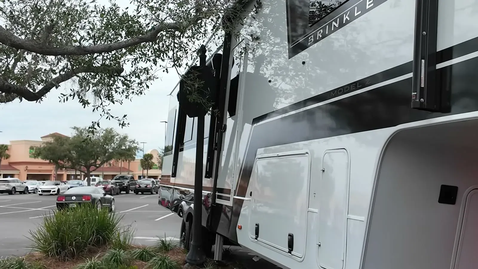 The fifth wheel wedged uncomfortably close to a tree and street sign on a tight parking lot corner.