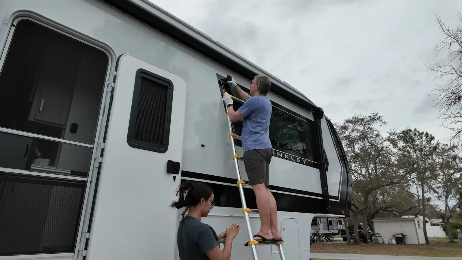 Nathan stands on the telescoping ladder to mount a camera above the window while Fabiola checks the view from below.