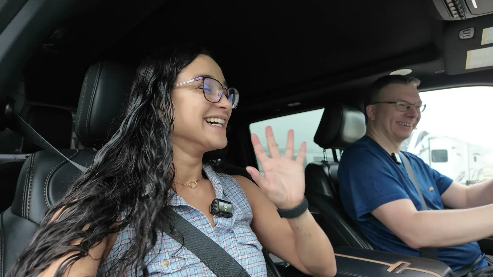 Fabiola in the passenger seat waving and Nathan driving the F-350 in the morning, with the fifth wheel visible through the window