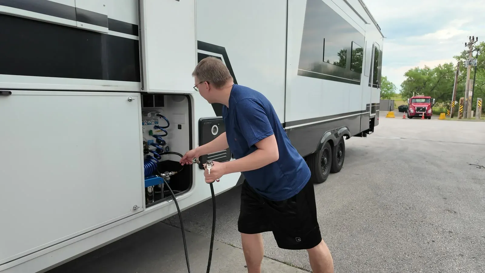 Nathan running a hose into the utility bay of the Brinkley fifth wheel to fill the fresh water tank at a truck stop