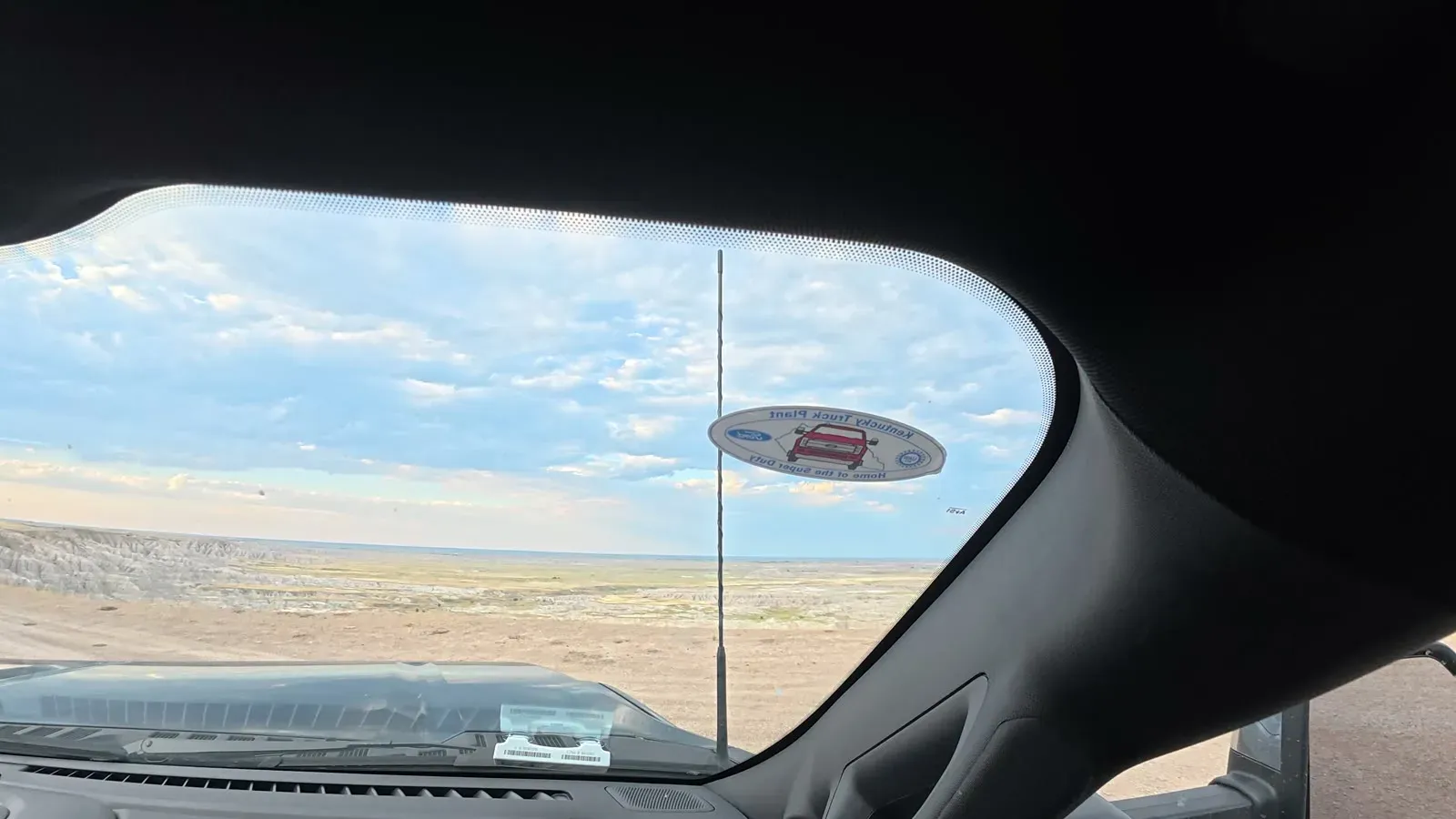 View through the truck windshield of the Badlands rock formation stretching across the horizon under a cloudy sky