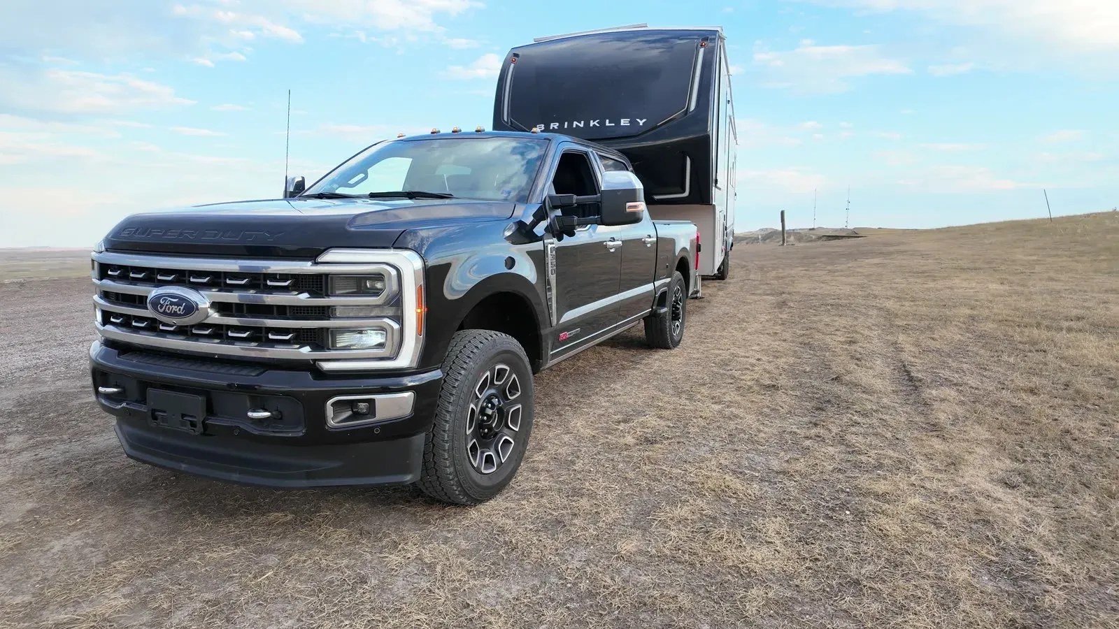 The black Ford F-350 hitched to the Brinkley fifth wheel parked on open grassland at the dispersed camping area near the Badlands
