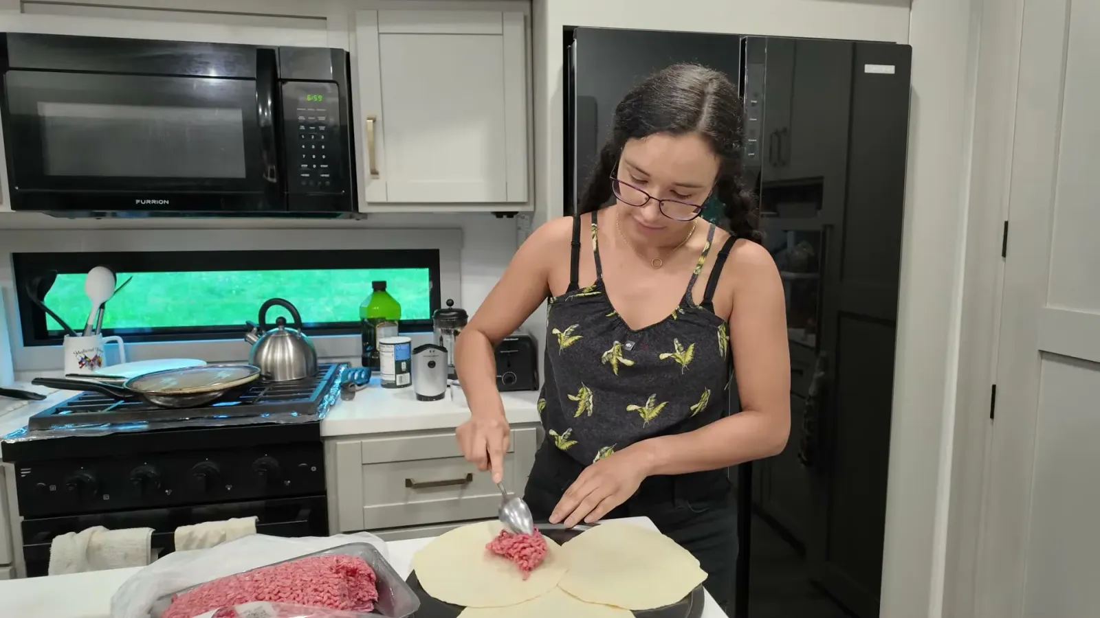 Spreading raw ground beef in a thin even layer across a flour tortilla with a spoon in the RV kitchen