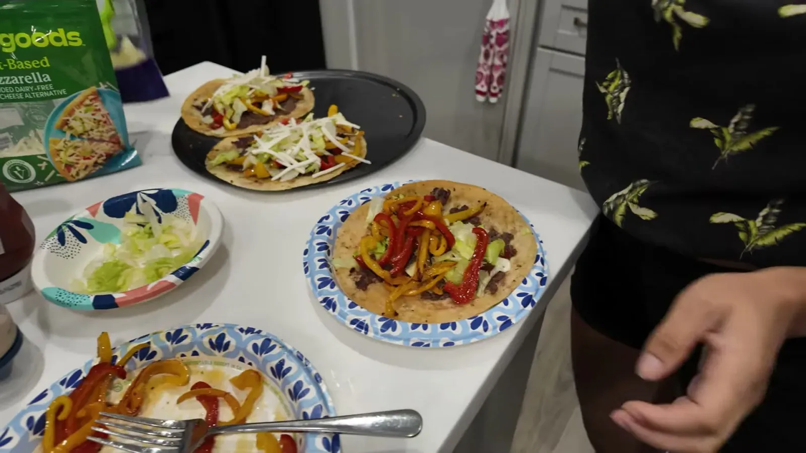 A finished Blackstone smash taco on a paper plate, topped with griddled red and yellow pepper strips and shredded lettuce, with more on a tray behind