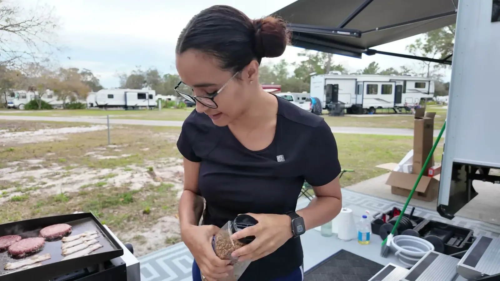 Strips of bacon and two raw burger patties cooking on the brand new Blackstone griddle at a Florida campsite