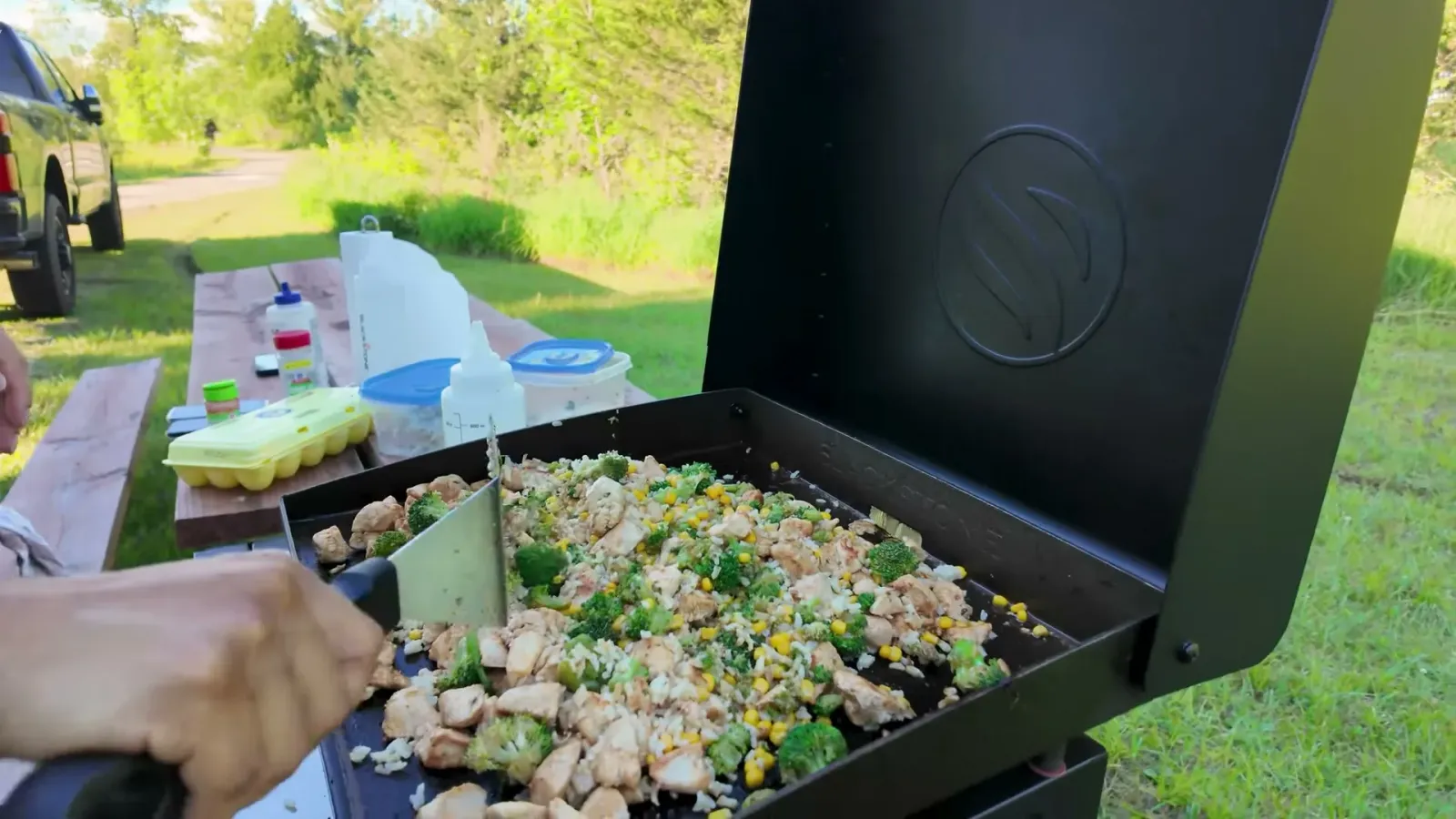 Chicken pieces browning on the Blackstone with chopped broccoli and corn added alongside